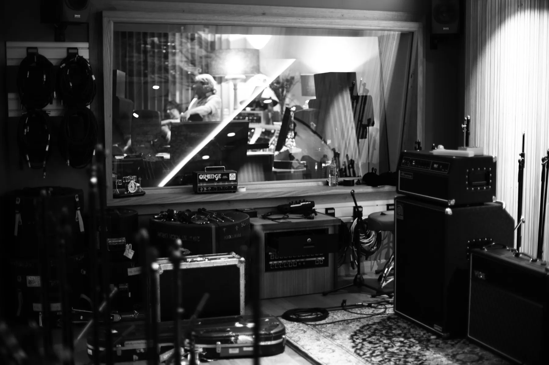 The A Sharp live room in black and white - amps, drum cases and the window through to a session in the control room